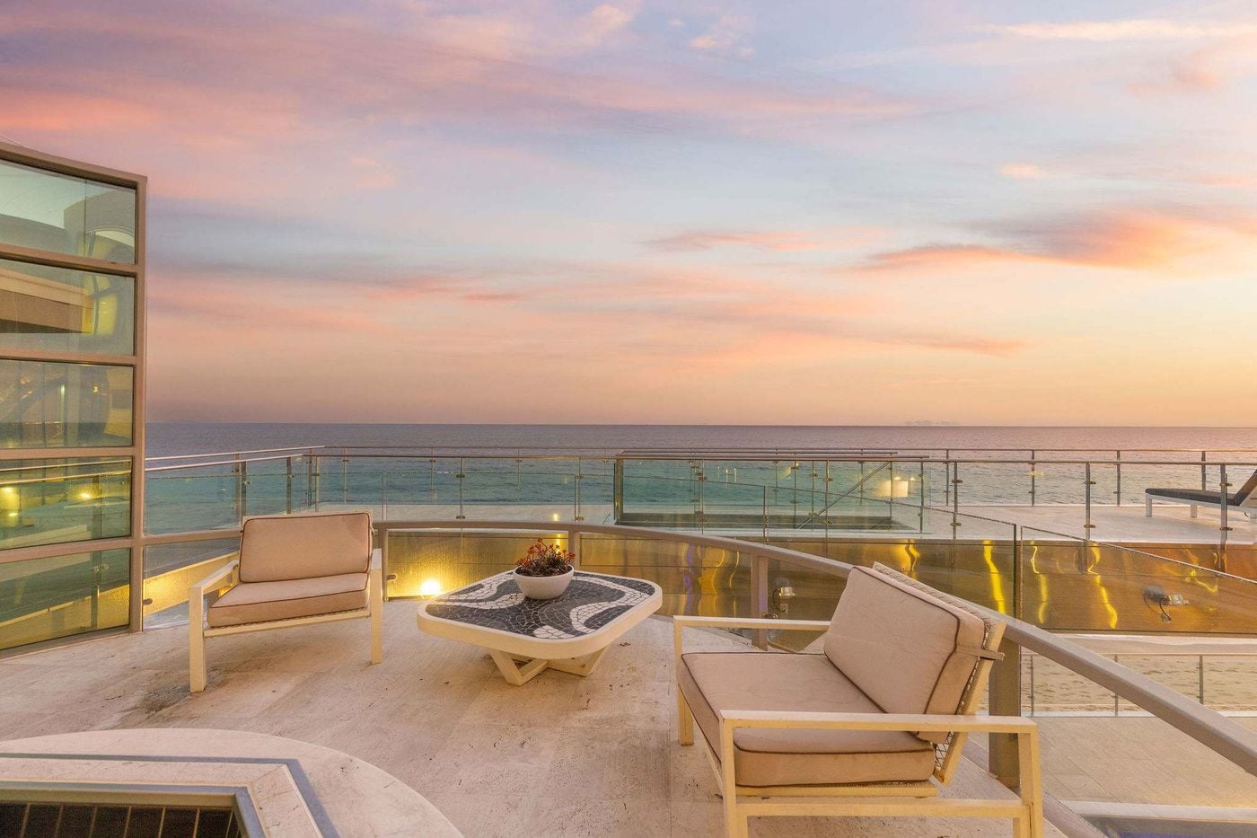 Oceanfront terrace with lounge chairs and glass railings overlooking the Pacific at dusk in Malibu