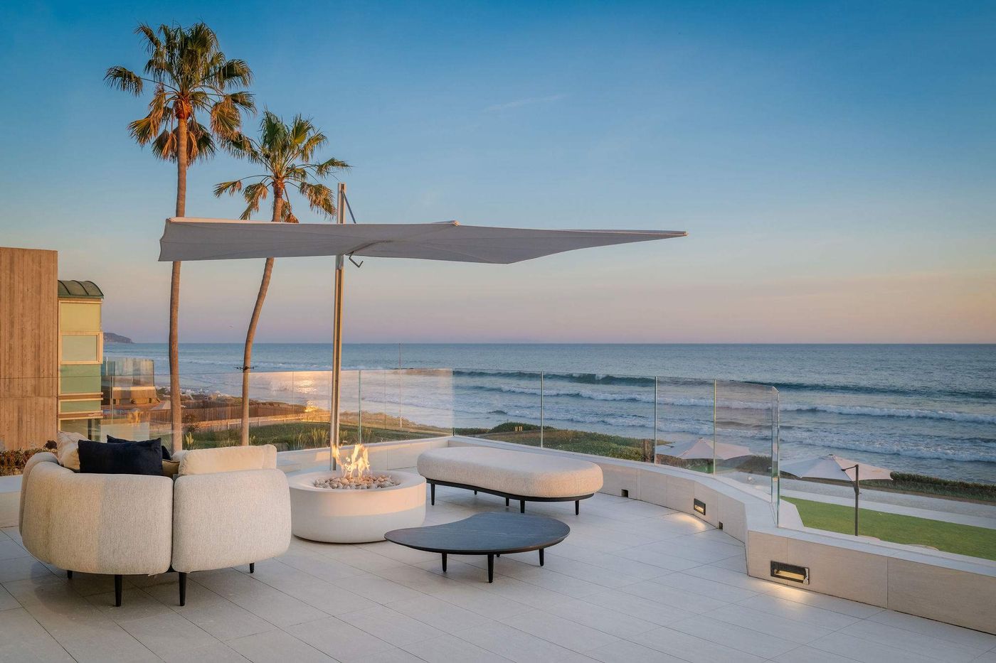 Beachside terrace with a lit fire table and lounge seating overlooking the Pacific at sunset in Malibu