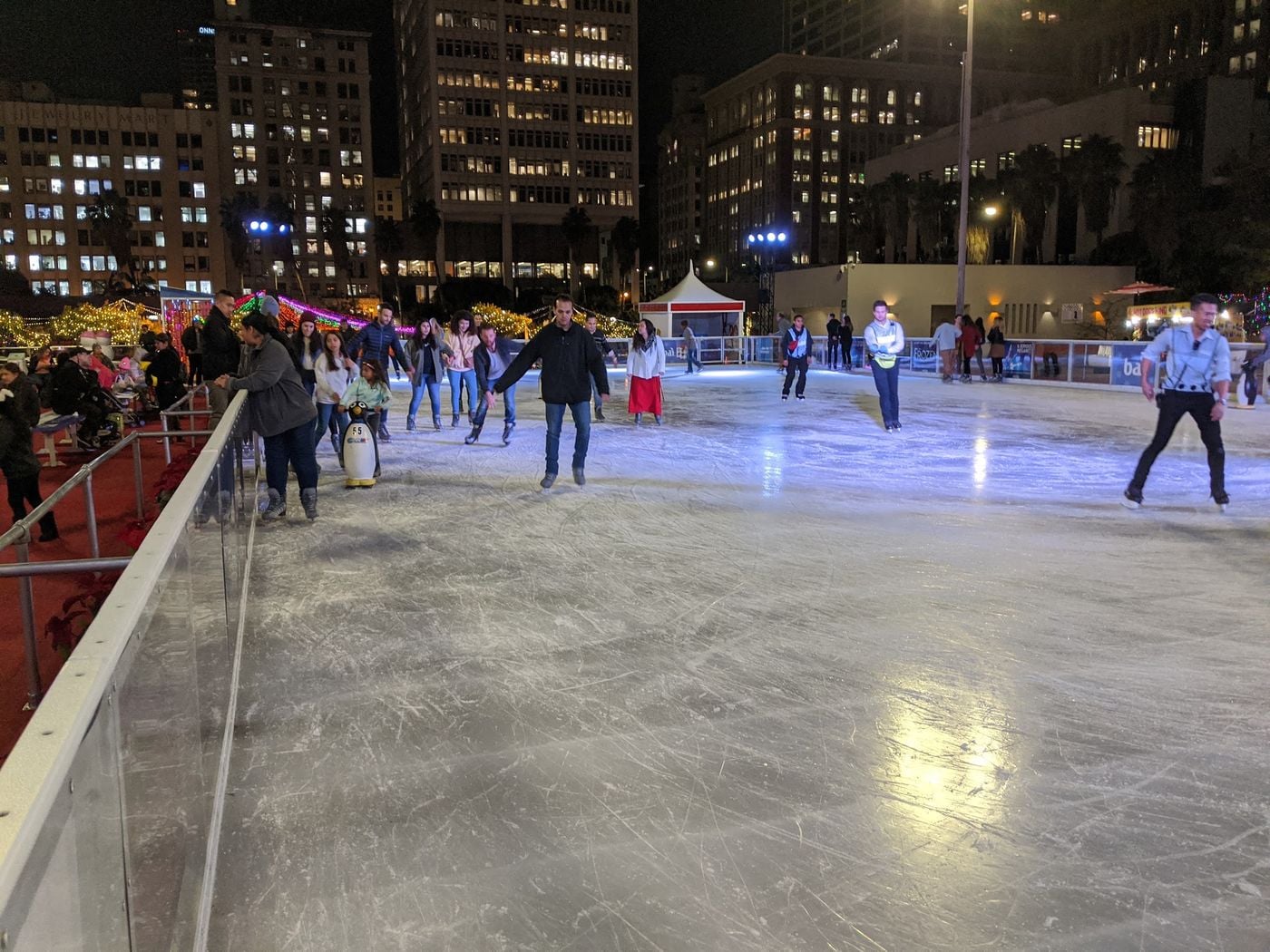 Skaters on the Holiday Ice Rink at Pershing Square at night, surrounded by downtown Los Angeles towers