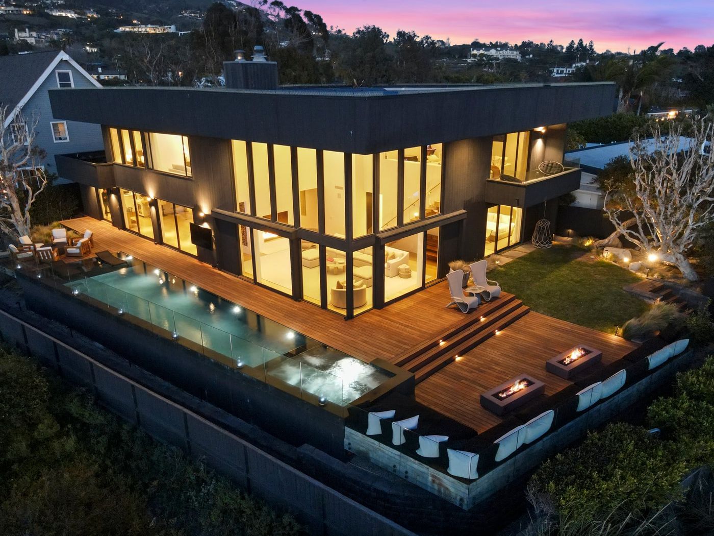 Modern Malibu home at dusk with an illuminated infinity pool and fire features on the deck