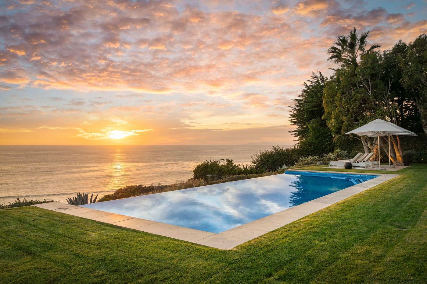 Infinity edge pool on a lawn above the Pacific Ocean at sunset in Malibu